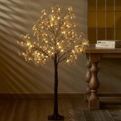 a lighted tree in the corner of a room next to a table with a book on it