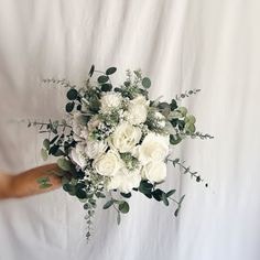 a bouquet of white roses and greenery in someone's hand on a white background