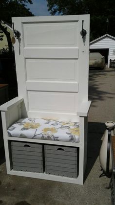 a white bench with storage drawers underneath it on the sidewalk next to a fenced in area