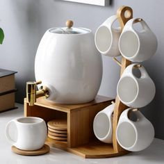 a white coffee pot and cups on a wooden stand next to a plant in a vase