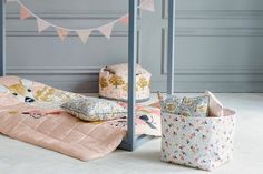 a bed with pink sheets and pillows on it next to two storage baskets in front of the bed