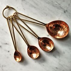 five brass spoons are lined up on a marble surface