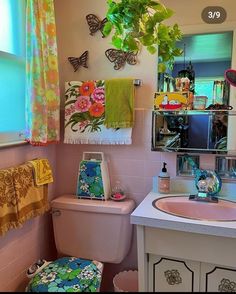 a bathroom with a pink toilet, sink and window covered in colorful towels hanging on the wall