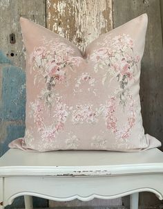 a pink pillow sitting on top of a white chair next to a wooden wall with peeling paint