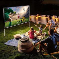 people sitting in lawn chairs watching television on the grass at night, with one person holding a remote control