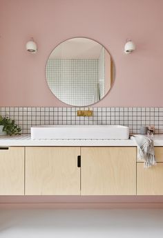 a bathroom with pink walls and white counter tops, along with a round mirror above the sink