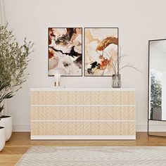 a white dresser sitting next to a mirror in a living room with two paintings on the wall