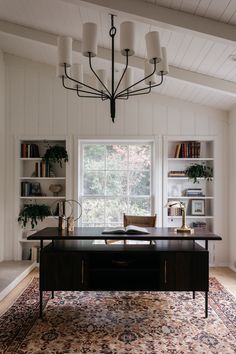 a room with a large rug, bookshelf and a desk in the middle