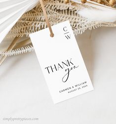 a white thank you tag hanging from a string next to some dried flowers and feathers