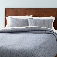 a bed with blue and white striped comforter on top of it next to a wooden headboard