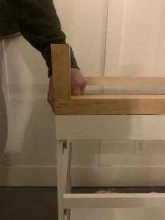 a person standing over a white table with drawers on it's sides and one hand reaching into the drawer