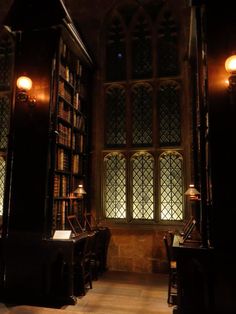 a dimly lit room with many bookshelves and desks in front of a window