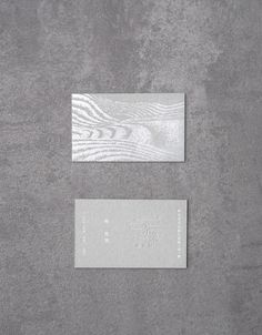 two white business cards sitting on top of a gray surface next to eachother