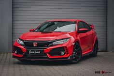 a red honda civic type car parked in front of a garage door with grey walls