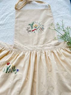 an apron with embroidered flowers on it sitting next to a potted plant and cloth