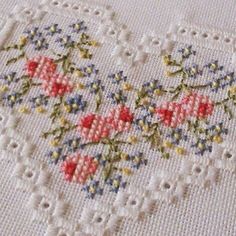 a close up of a cross stitched heart on a white cloth with red, yellow and blue flowers