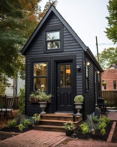 a small black house with two windows and steps leading to the front door is surrounded by greenery