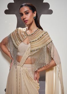 Embodying strength and style, our Tatiana sari set seamlessly combines effortless silhouettes, elegant drapery, delicate embroidery, and distinctive fringe details to create a look that is both soft and resilient. Traditional Draped Hand Embellished Lehenga, Elegant Designer Choli With Cape Sleeves, Bollywood Style Hand Embellished Traditional Blouse Piece, Elegant Draped Sets For Diwali, Festive Hand Embellished Draped Saree, Elegant Eid Sets With Tassels, Beige Party Sets With Traditional Drape, Designer Draped Hand Embellished Saree, Elegant Beige Choli With Traditional Drape