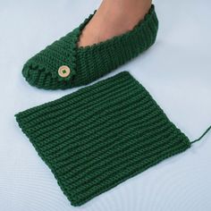 a pair of green knitted slippers sitting on top of a white bed next to a woman's foot