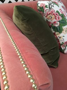 the back of a pink couch with gold beading and pillows on top of it