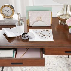 a wooden desk topped with lots of clutter next to a clock and other items