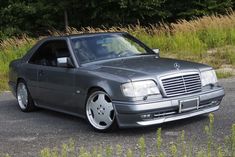 a mercedes benz is parked on the side of the road in front of some tall grass