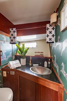 a bathroom with green and white wallpaper, wood cabinetry, sink and toilet