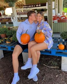 a man and woman sitting on a blue bench with pumpkins in front of them