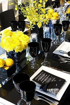 the table is set with black and white dishes, silverware, and yellow flowers