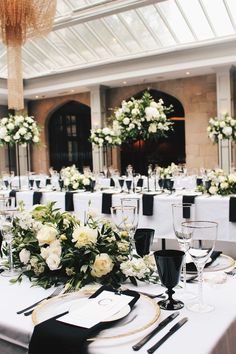 the table is set with white flowers and black place settings for an elegant wedding reception