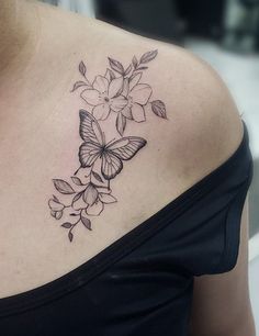 a woman with a butterfly and flowers tattoo on her upper back shoulder is looking at the camera