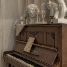 an old piano with statues on top of it in front of a curtained window