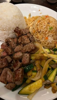 a white plate topped with meat and veggies next to rice on top of a table