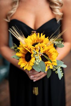 a woman in a black dress holding a bouquet of sunflowers