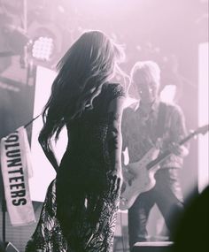 a woman standing on top of a stage next to a man with a guitar in her hand