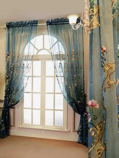 a window with blue curtains and flowers on the windowsill, in front of a chandelier