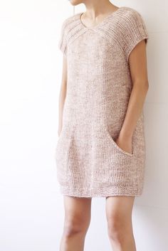 a woman standing in front of a white wall wearing a sweater dress with an open back