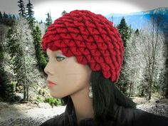 a mannequin head wearing a red knitted hat in front of some trees