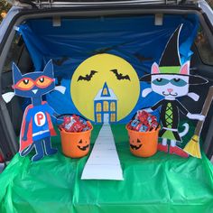 the trunk of a car is decorated with halloween decorations and paper cutouts, along with two buckets filled with candy