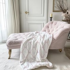 a pink chaise lounge chair with a white blanket on it in front of a window