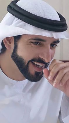 a man with a beard is smiling and pointing to the side while wearing a white hat