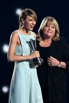 two women standing next to each other on stage with one holding an award in her hand