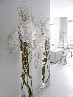 two tall vases filled with white flowers on top of a wooden floor next to a wall