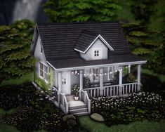 a small white house surrounded by greenery and trees with lights on the front porch