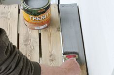 a man is painting the side of a wooden bench with a paint can and brush