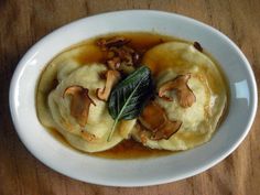 a white plate topped with dumplings covered in sauce and toppings on top of a wooden table