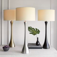 three lamps on a table with a plant in the middle and a vase next to them