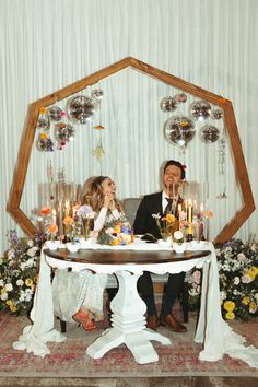 a man and woman sitting at a table in front of some balloons with candles on it