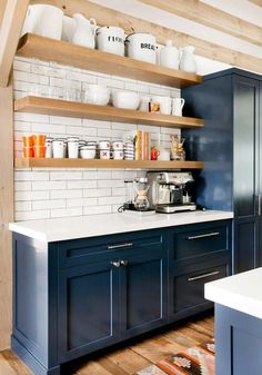 a kitchen with blue cabinets and white subway tile backsplash, wooden shelves above the sink