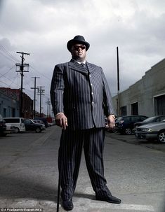 a man in a pinstripe suit and hat standing on the side of a road